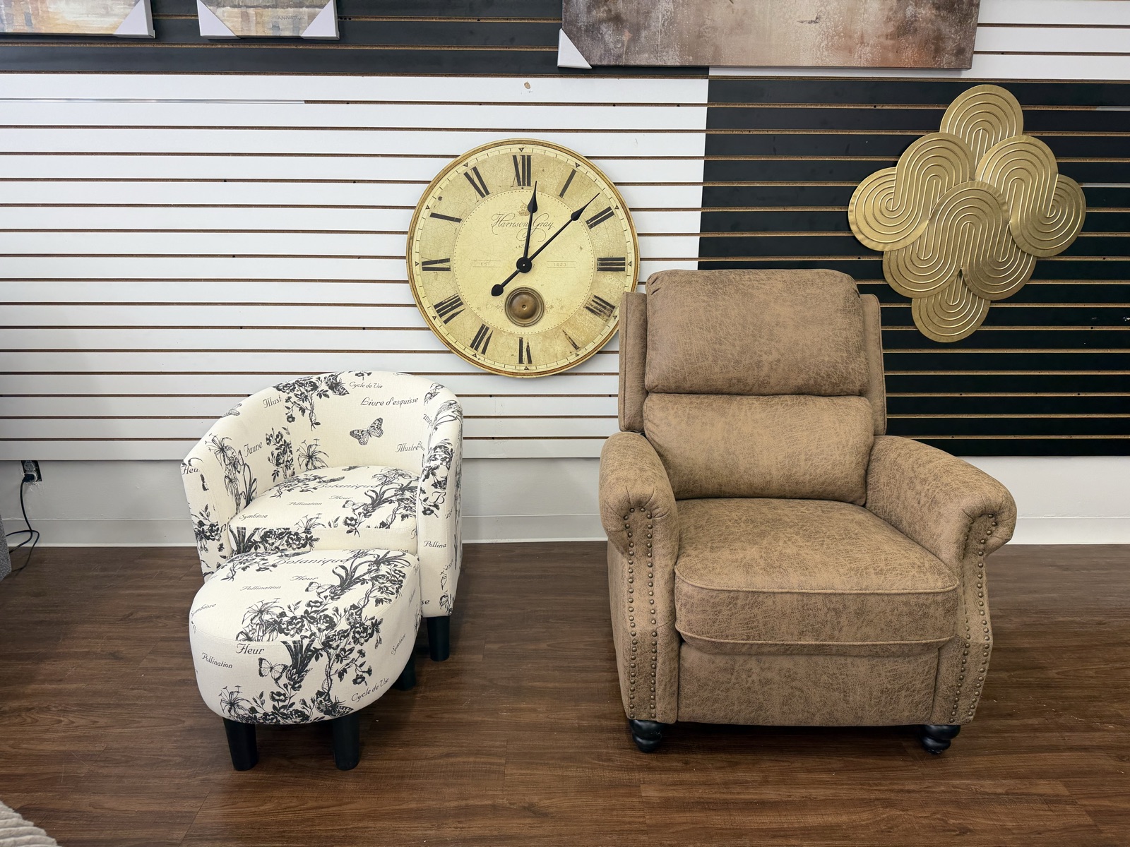 Botanical-print barrel accent chair with ottoman, staged beside a tan nailhead recliner under a large wall clock.