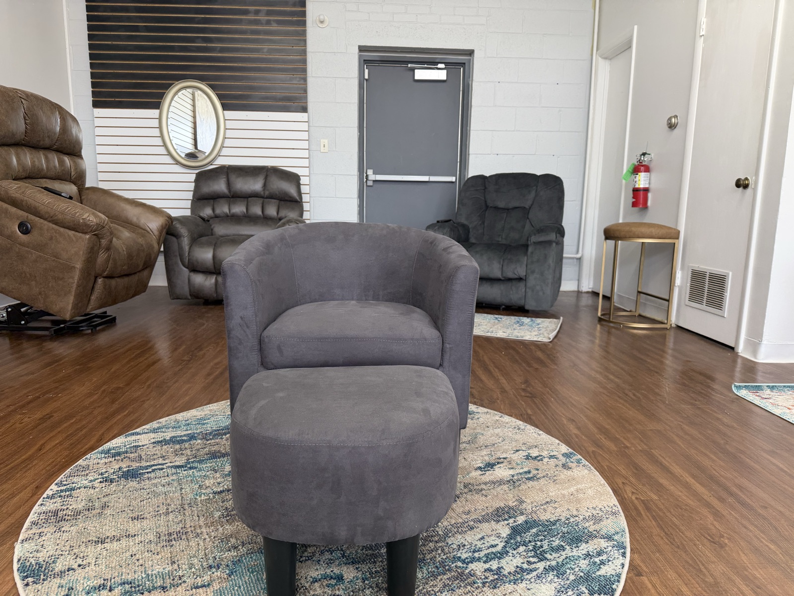 Gray swivel barrel accent chair with a matching round ottoman on a blue patterned round rug.
