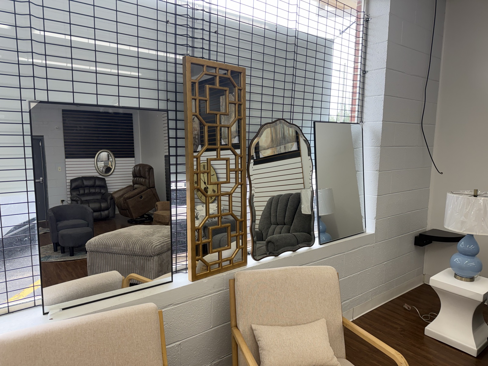 A grouping of accent mirrors — a tall gold geometric mirror, an arched mirror, and large beveled mirrors — displayed on the showroom wall.