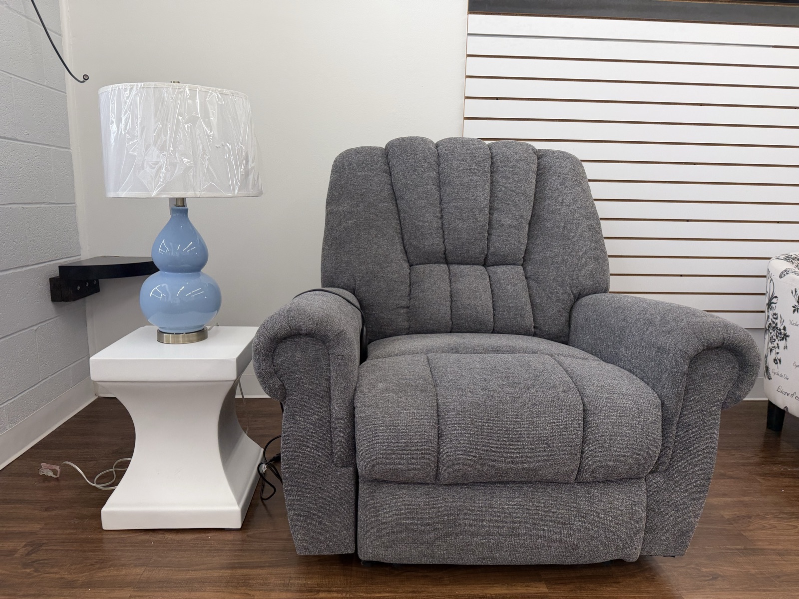 Gray channel-back recliner staged beside a white pedestal accent table and a blue gourd lamp.