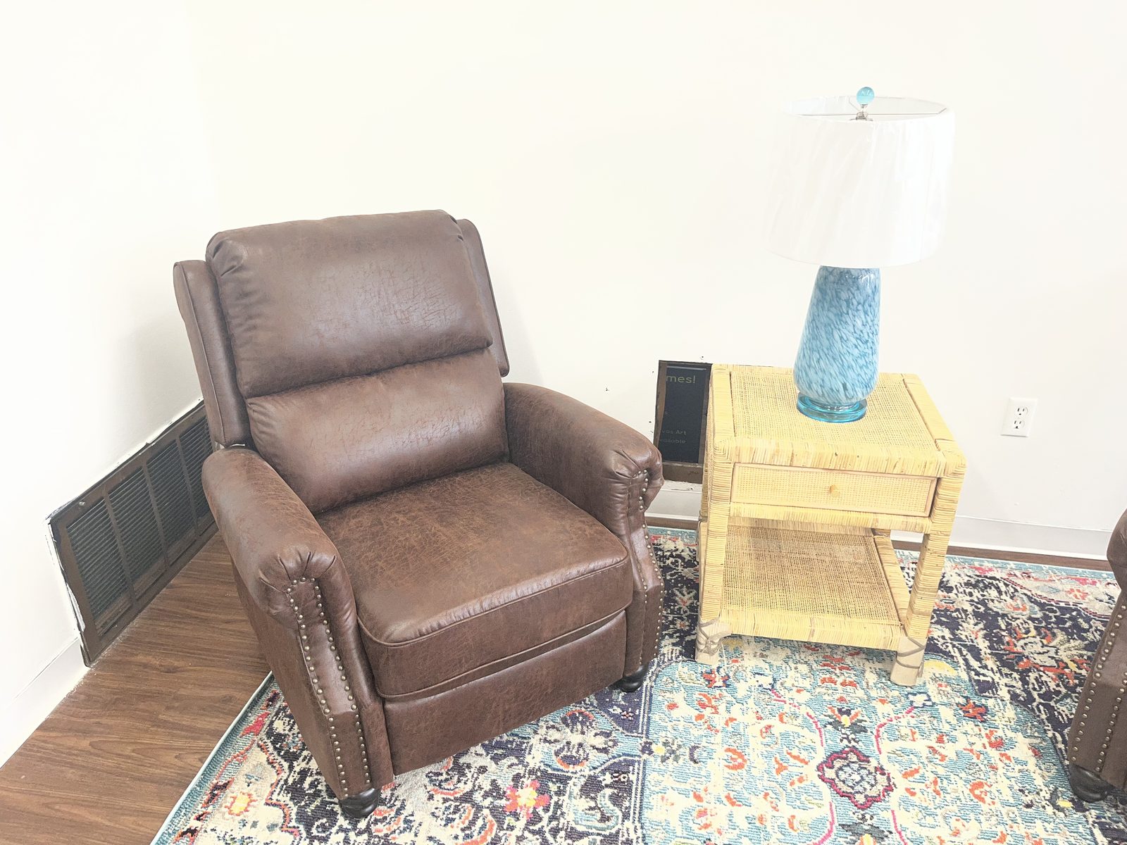 Brown nailhead-trim recliner staged with a rattan side table, blue ceramic lamp, and a patterned area rug.